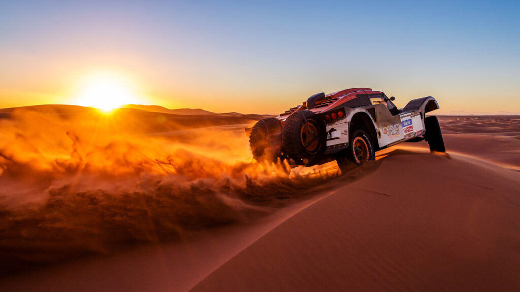 Red rally car drifting on sand dunes at sunset – desert rally photography by Zypix Dubai